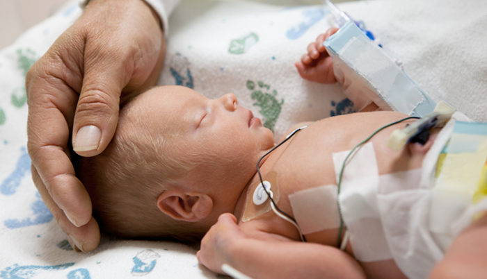Father Touching Head Of A Premature Baby In Incubator