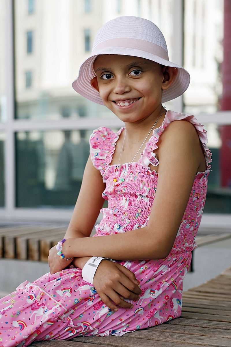 CHoR patient Estrella in a sundress and hat sitting outside