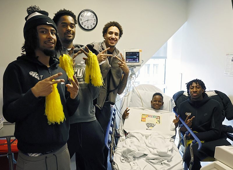 Rams basketball players smile with a CHoR patient in his room